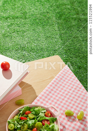Template photo with summertime style, in the corner is a table of wood containing vegetable salad dish and some books, decorated with a pink carpet. Empty space on table and lawn for designing 115521994