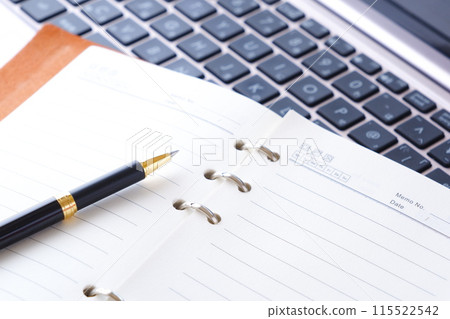 某人在筆記型電腦上進行辦公桌工作的圖片，其中環形筆記本打開。 115522542