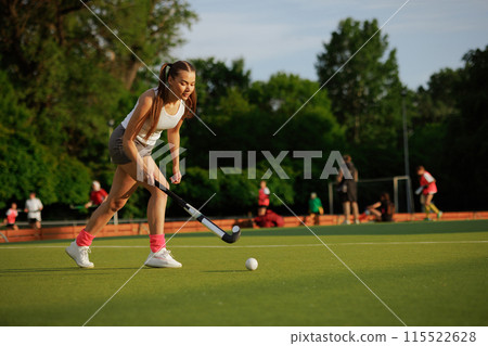 girl hockey player plays field hockey on a sunny day, the hockey player hits the ball with a stick 115522628