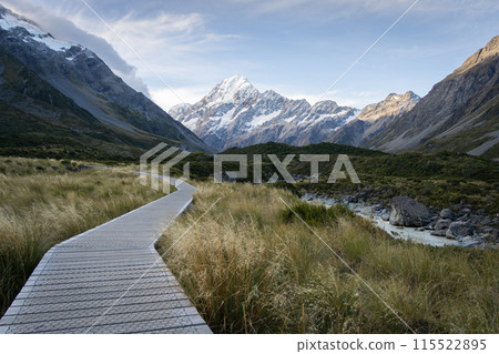 Wooden boardwalk leading through beautiful alpine valley with snowy mountain in backdrop,New Zealand Wooden boardwalk leading through beautiful alpine valley with snowy mountain in backdrop,New Zealand 115522895