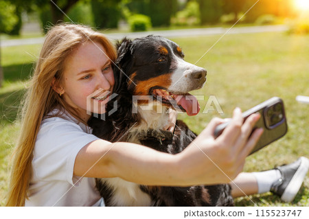 A woman is taking a selfie with her dog outdoors, both looking happy A woman is taking a selfie with her dog outdoors, both looking happy 115523747