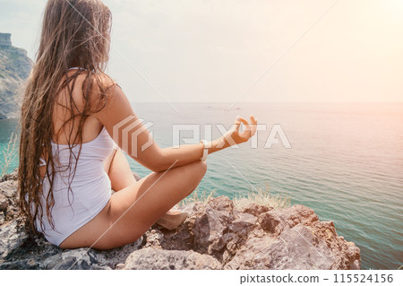 Woman sea yoga. Back view of free calm bliss satisfied woman with long hair standing on top rock with yoga position against of sky by the sea. Healthy lifestyle outdoors in nature, fitness concept. Woman sea yoga. Back view of free calm bliss satisfied woman with long hair standing on top rock with yoga position against of sky by the sea. Healthy lifestyle outdoors in nature, fitness concept. 115524156