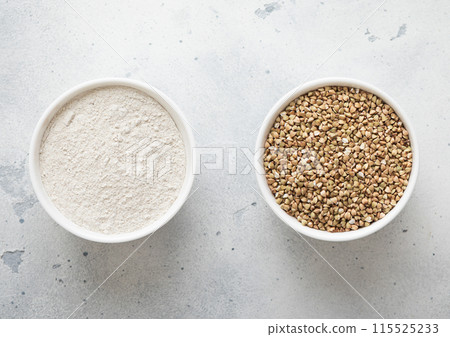 Bowls plates with green dry raw buckwheat seeds and flour powder on kitchen table. Bowls plates with green dry raw buckwheat seeds and flour powder on kitchen table. 115525233