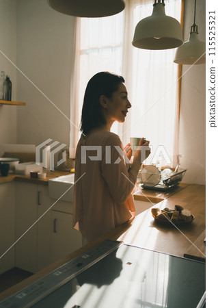 一位 40 多歲的家庭主婦在廚房裡拿著杯子 一位 40 多歲的家庭主婦在廚房裡拿著杯子 115525321