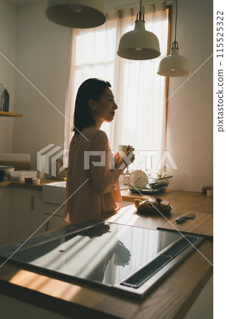 一位 40 多歲的家庭主婦在廚房裡拿著杯子 一位 40 多歲的家庭主婦在廚房裡拿著杯子 115525322