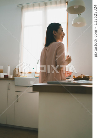 一位 40 多歲的家庭主婦在廚房裡拿著杯子 一位 40 多歲的家庭主婦在廚房裡拿著杯子 115525324