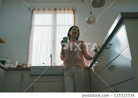 一位 40 多歲的女性在廚房裡拿著杯子放鬆 一位 40 多歲的女性在廚房裡拿著杯子放鬆 115525336