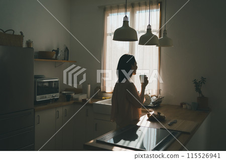 一位 40 多歲的家庭主婦在廚房裡拿著杯子 一位 40 多歲的家庭主婦在廚房裡拿著杯子 115526941