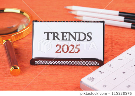 2025 trend concept. TRENDS 2025 on a white business card in a stand with a magnifying glass, pencils and a calculator 2025 trend concept. TRENDS 2025 on a white business card in a stand with a magnifying glass, pencils and a calculator 115528576