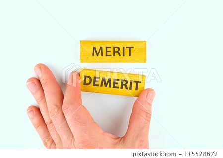 Business and demerit or merit concept. Copy space. Concept word Demerit or Merit on wooden blocks on a light background laid out with the help of a hand Business and demerit or merit concept. Copy space. Concept word Demerit or Merit on wooden blocks on a light background laid out with the help of a hand 115528672