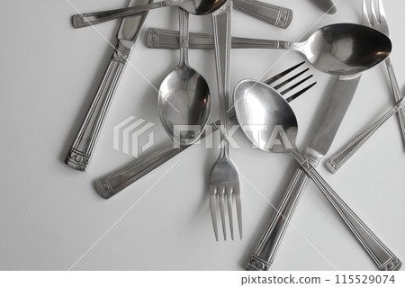 Table Knives, Tablespoons And Fork Chaotically Scattered On White Table Stock Photo Table Knives, Tablespoons And Fork Chaotically Scattered On White Table Stock Photo 115529074