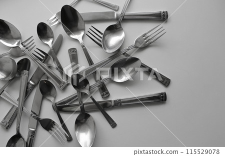 Variety size spoons, forks and table knives scattered on white surface at a side of image Variety size spoons, forks and table knives scattered on white surface at a side of image 115529078