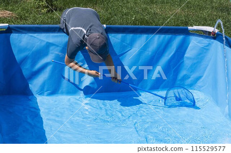 Boy diligently skimming leaves and debris from a sparkling blue pool, illustrating the routine upkeep required to maintain clarity and cleanliness 115529577
