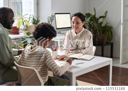 Portrait of smiling young woman as psychologist helping Black family in therapy session with young child drawing pictures Portrait of smiling young woman as psychologist helping Black family in therapy session with young child drawing pictures 115531188
