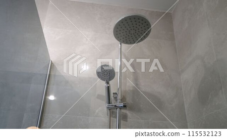 Fragment of a shower head against the background of brown ceramic tiles in the bathroom, close-up. Shower close-up without water. Fragment of a shower head against the background of brown ceramic tiles in the bathroom, close-up. Shower close-up without water. 115532123
