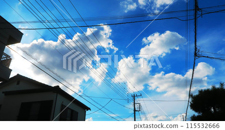 A landscape of electric wires and telegraph poles in a residential area with blue sky and clouds 115532666