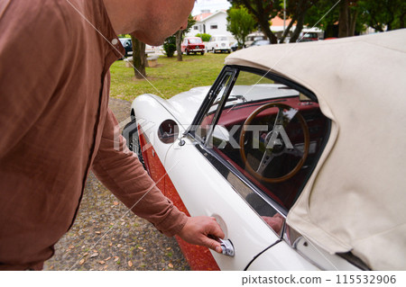 A stylish man in a shirt holds on to the handle of a retro car. A stylish man in a shirt holds on to the handle of a retro car. 115532906