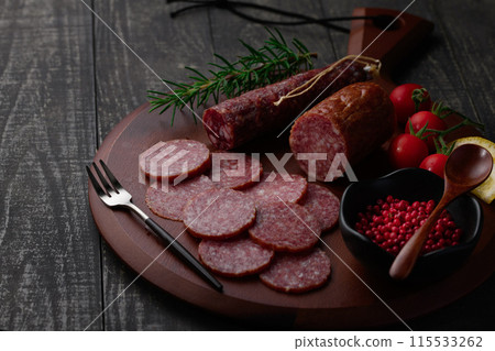Matured salami on a cutting board with pink pepper, rosemary, cherry tomatoes and lemon 115533262