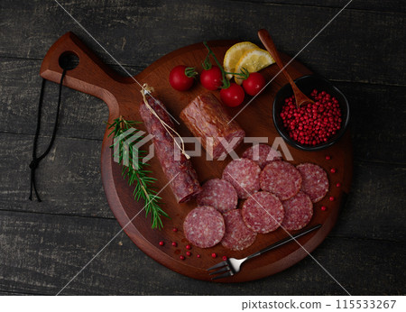 Matured salami on a cutting board with pink pepper, rosemary, cherry tomatoes and lemon Matured salami on a cutting board with pink pepper, rosemary, cherry tomatoes and lemon 115533267