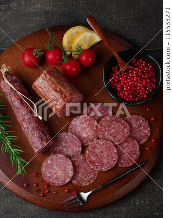 Matured salami on a cutting board with pink pepper, rosemary, cherry tomatoes and lemon 115533271