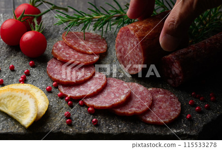 Matured salami on a cutting board with pink pepper, rosemary, cherry tomatoes and lemon 115533278