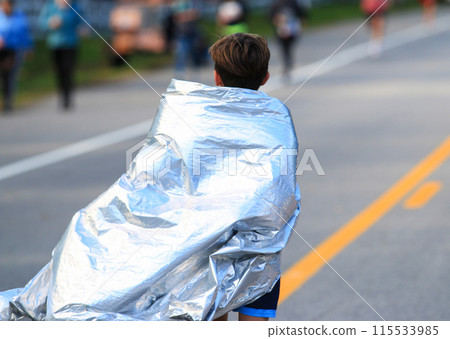 Close up of Young runner wearing a foil blanket after running a road race in the fall from behind Close up of Young runner wearing a foil blanket after running a road race in the fall from behind 115533985