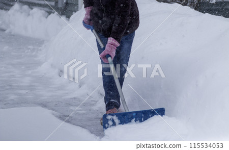 Women shoveling two feet of snow off her driveway wearing pink gloves Women shoveling two feet of snow off her driveway wearing pink gloves 115534053
