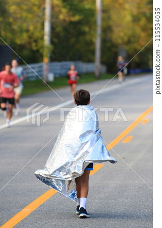 Young runner wearing a foil blanket after running a road race in the fall Young runner wearing a foil blanket after running a road race in the fall 115534055