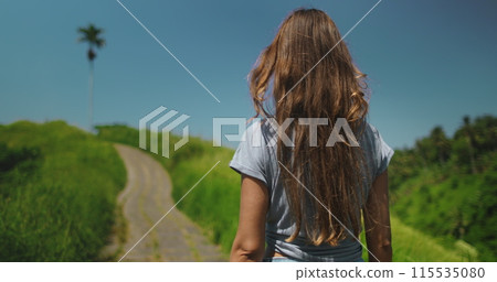 Tourist woman walking Campuhan Ridge Walk - tourist place to visit in Ubud, Bali island. Green field, blue sky. Outdoor lifestyle travel on summer holiday vacation. Close up back view 115535080