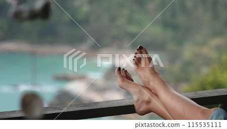 A person is seen resting comfortably with their feet propped up on a metal railing in an urban setting. 115535111