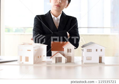 A worried woman in a suit thinking in front of a model house A worried woman in a suit thinking in front of a model house 115535721