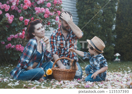 young parents - dad, mom and son in plaid shirts and jeans are sitting on a picnic in the garden young parents - dad, mom and son in plaid shirts and jeans are sitting on a picnic in the garden 115537393