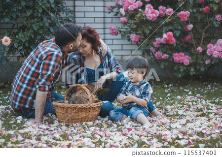 young parents - dad, mom and son in plaid shirts and jeans are sitting on a picnic in the garden 115537401