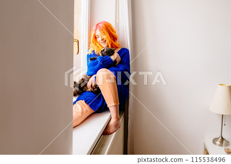 Cheerful woman with orange hair is holding a cat in her arms. The cat is black and white. The woman is smiling and she is happy Cheerful woman with orange hair is holding a cat in her arms. The cat is black and white. The woman is smiling and she is happy 115538496