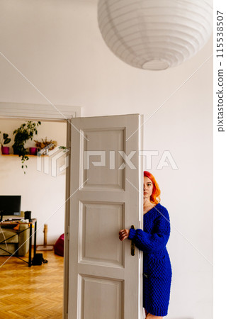 Vertical shot of sad woman with bright color hairstyle blue knitted dress, a white door hiding half face. concept of anxiety, loneliness, depression 115538507