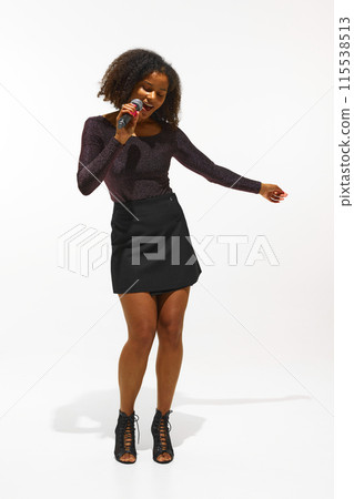 Young woman, singer in fashionable attire singing in microphone isolated on white background. Music and Fashion 115538513