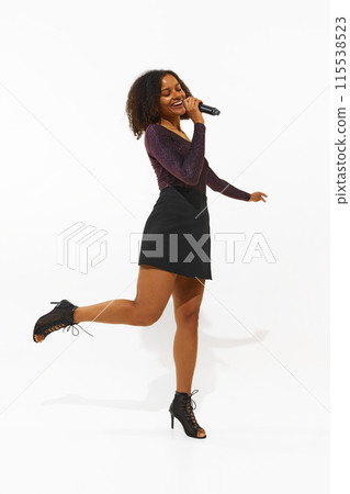 Full-length of African-American woman, young singer in a sparkling top and mini skirt performs with a microphone isolated on white background 115538523