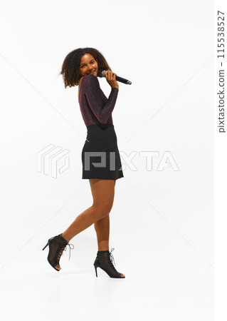 Full-length of African-American woman, young singer in a sparkling top and mini skirt performs with a microphone isolated on white background Full-length of African-American woman, young singer in a sparkling top and mini skirt performs with a microphone isolated on white background 115538527