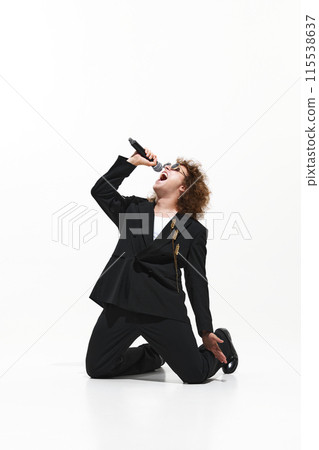 Rockstar Moment. Young man with curly hair, in black suit energetically and passionately singing isolated on white background 115538637
