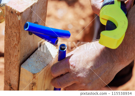 Plumber using saw tools to cut plastic blue PVC water piping system 115538934