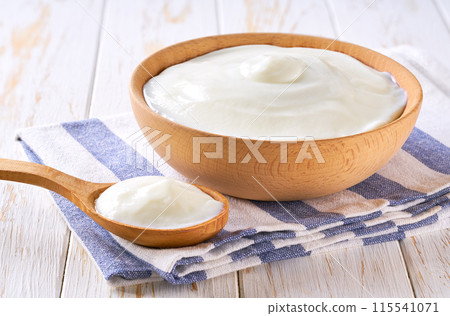 Greek yogurt or sour cream in a wooden bowl with spoon on a light table, selective focus. Greek yogurt or sour cream in a wooden bowl with spoon on a light table, selective focus. 115541071