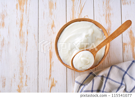 Greek yogurt or sour cream in a wooden bowl with spoon on a light table, top view. 115541077