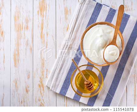 Greek yogurt or sour cream in a wooden bowl and jar of honey on light table, top view. 115541078