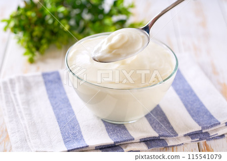 Tasty yogurt in a bowl with spoon on a white table, selective focus. 115541079