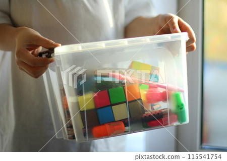 the child holds a box with educational games, puzzles, pencils. preparation for a creative activity 115541754