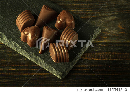 Dark chocolate candies on a serving board. Space for advertising on vintage black table 115541840