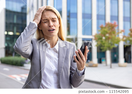 Worried and upset young business woman standing outside on the street in a suit, holding a mobile phone and holding her head with her hand in disappointment, got bad news. Worried and upset young business woman standing outside on the street in a suit, holding a mobile phone and holding her head with her hand in disappointment, got bad news. 115542095