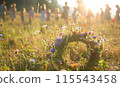 Wildflowers wreath on a sunny meadow. Sunny green natural background. Summer solstice concept. Symbol of Beltane. 115543458