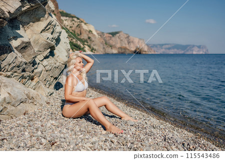 A blonde woman is sitting on a beach with her hair in her hand 115543486