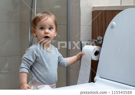 Toddler ripping up toilet paper in bathroom. Concept of naughty baby 115543589